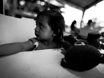 Baby girl sitting with teddy bear at table in restaurant