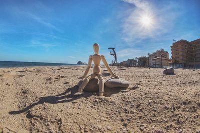 Rear view of man sitting on beach against sky on sunny day