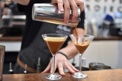 Midsection of bartender pouring cocktail in martini glass