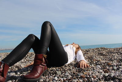 Woman lying on pebbles at beach against sky