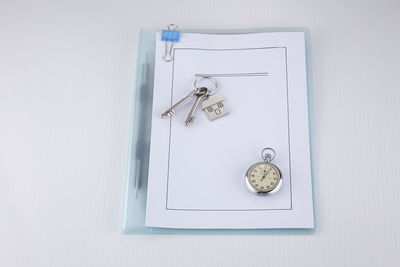 High angle view of house key and pocket watch on document