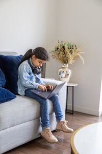 Girl using laptop while sitting on sofa at home