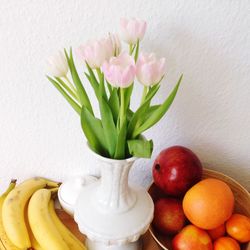 Pink tulips in vase amidst fruits on table