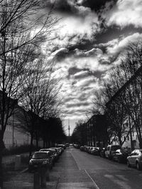 Road passing through bare trees against cloudy sky