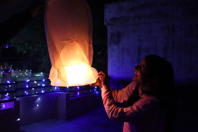 Side view of young woman holding illuminated lamp at night