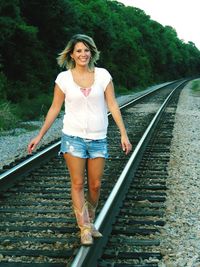 Portrait of beautiful woman standing on railroad track against trees