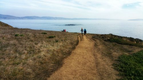 Rear view of people walking on footpath by sea