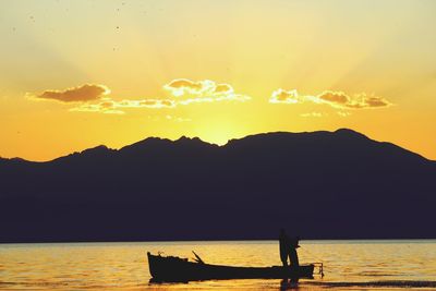 Silhouette man by sea against sky during sunset