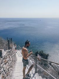 Man standing on railing against sea