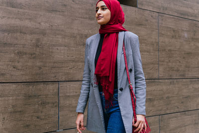 Content young arab female wearing traditional hijab and casual clothes walking along city street and looking forward