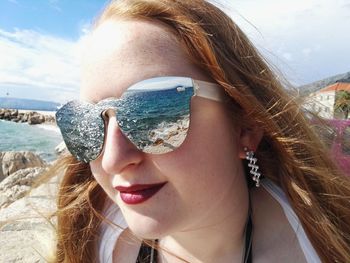 Beautiful young woman in sunglasses at beach against sky