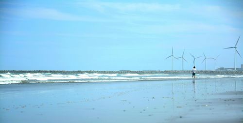 Man standing at beach by windmills against sky