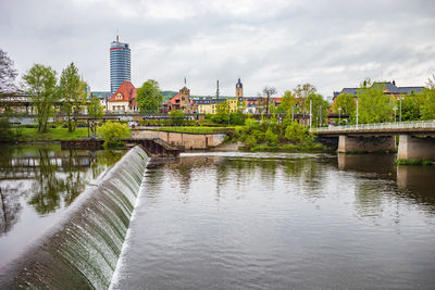 Bridge over river by buildings against sky