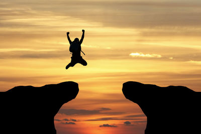 Silhouette man jumping against orange sky during sunset