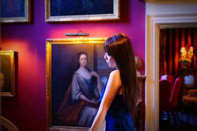Side view of teenage girl wearing dress standing against paintings