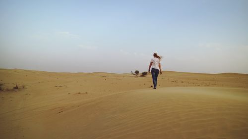 Rear view of woman walking at desert against clear sky