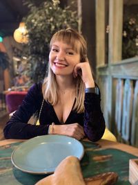 Portrait of happy young woman sitting at table in restaurant