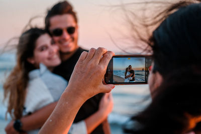 Woman taking a photo of two young adults using a mobile phone