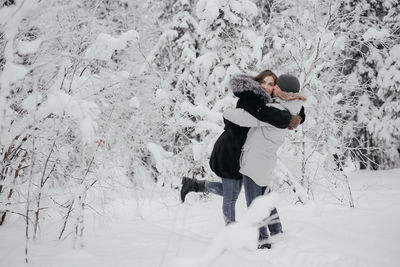 Beautiful young european couple in a sweater in winter in the forest hugging, kissing.