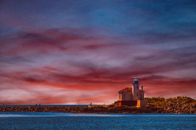 Lighthouse by sea against sky during sunset