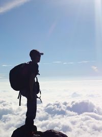 Side view of man with backpack standing on cliff against sky