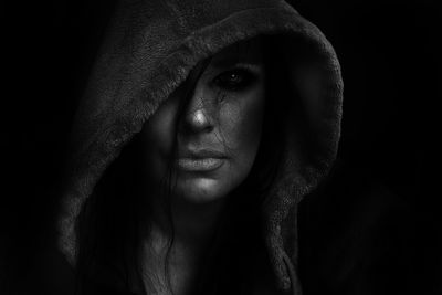 Close-up of young hooded woman against black background