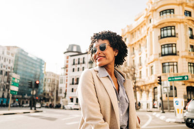 Young woman wearing sunglasses standing against city