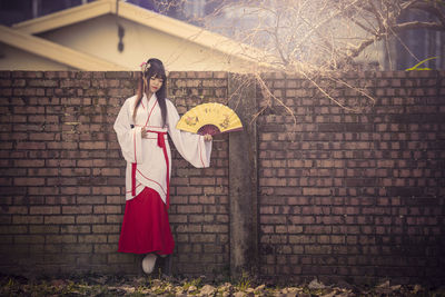 Woman with umbrella standing against brick wall