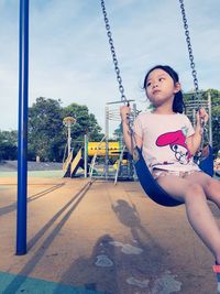Girl looking away while sitting on swing at playground