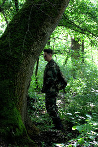 Boy standing by tree trunk in forest