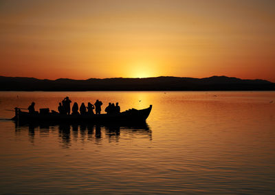 Silhouette people on boat in lake against sky during sunset