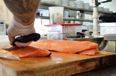Cropped hand of chef wearing glove cutting fish in kitchen