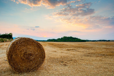 Hay bale on field against sky during sunset