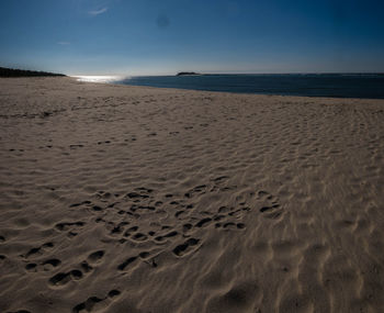 Footprints on sand at beach against sky