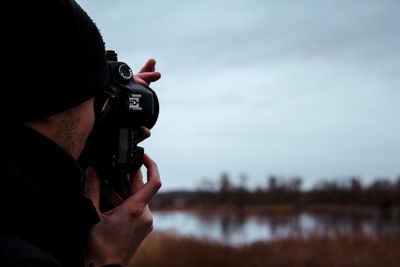 Man photographing through camera against sky