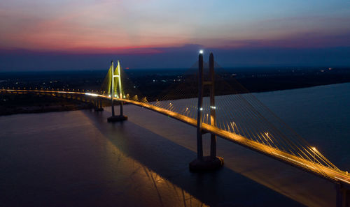 Illuminated bridge over river against sky at sunset