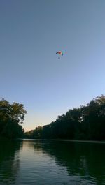 Person paragliding over river against clear sky