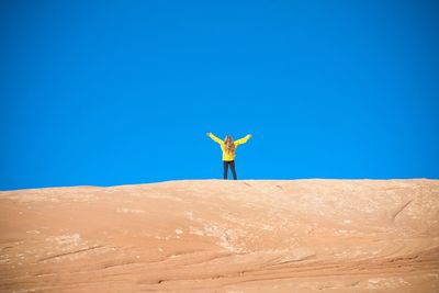 Woman standing in desert against clear blue sky