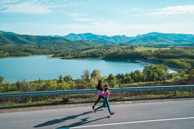 Full length of woman running on road by lake against sky