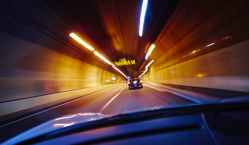 Car moving in illuminated tunnel seen from windshield