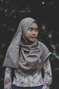 Teenager girl looking away while standing against tree