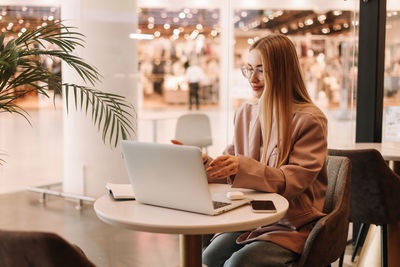 Portrait of a business woman student with glasses drinking coffee working using laptop in cafe 