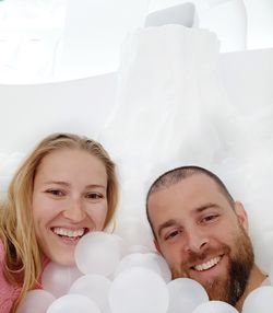 Portrait of smiling mid adult couples with white balloons on bed at home