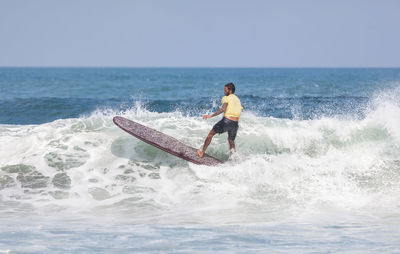 Rear view of man surfing in sea against sky