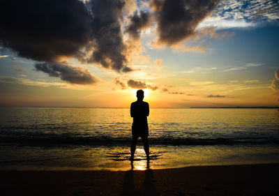 Silhouette man standing at beach against sky during sunset