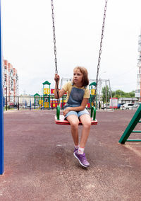 Full length of a girl sitting on swing at playground
