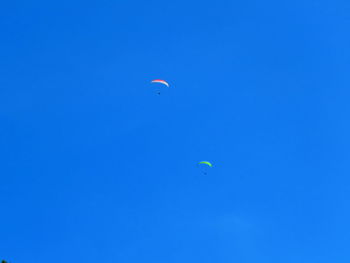 Low angle view of 2 paragliders against blue sky