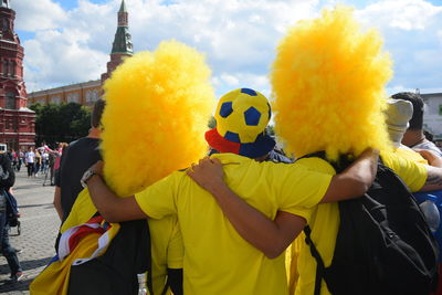 Rear view of fans standing on city street against cloudy sky