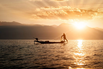 Silhouette person in sea against sky during sunset