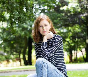 Portrait of beautiful young woman sitting against trees